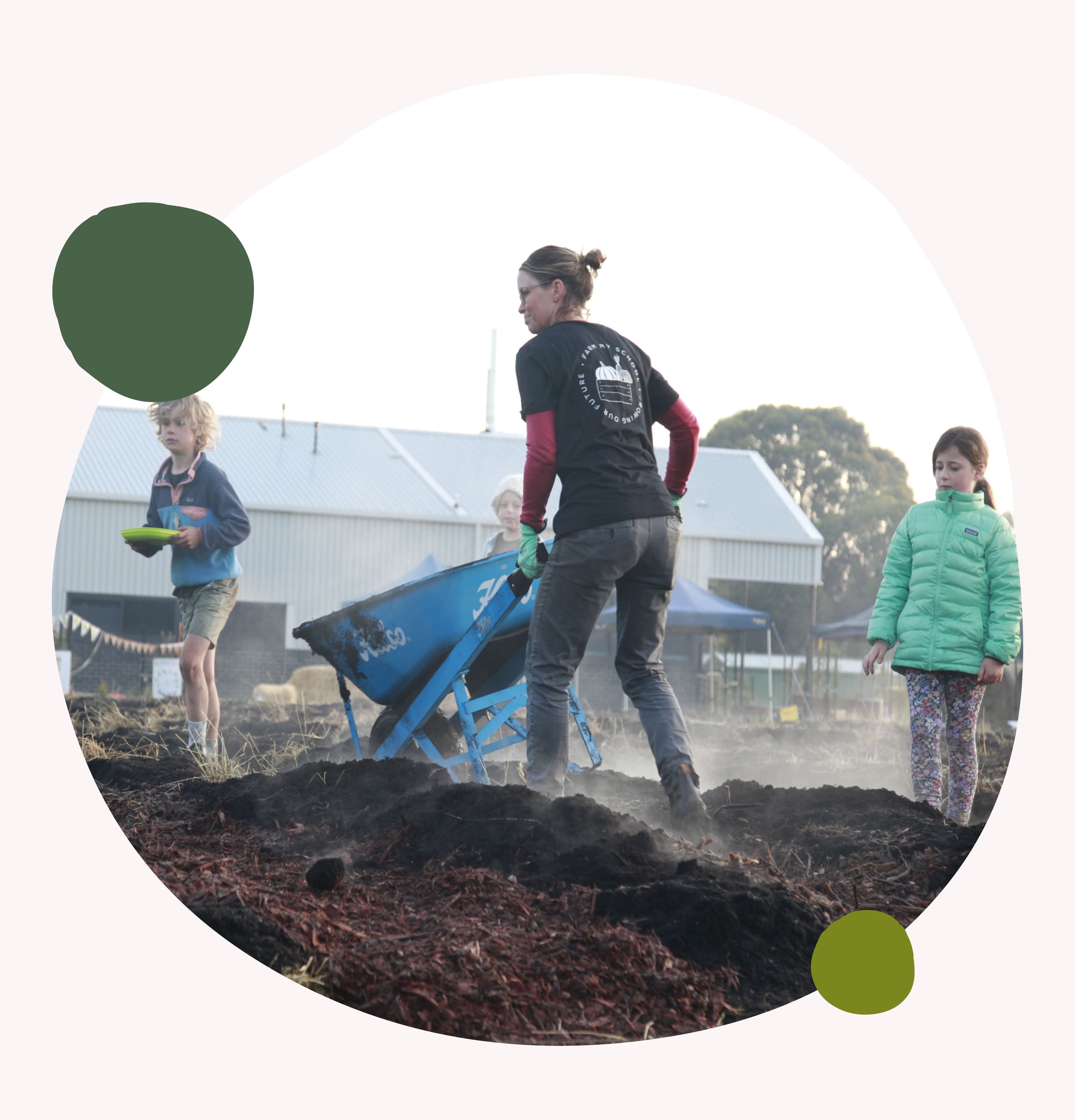 Farmer and volunteer with wheelbarrow and students preparing soil at a school farm, promoting education and community food systems.