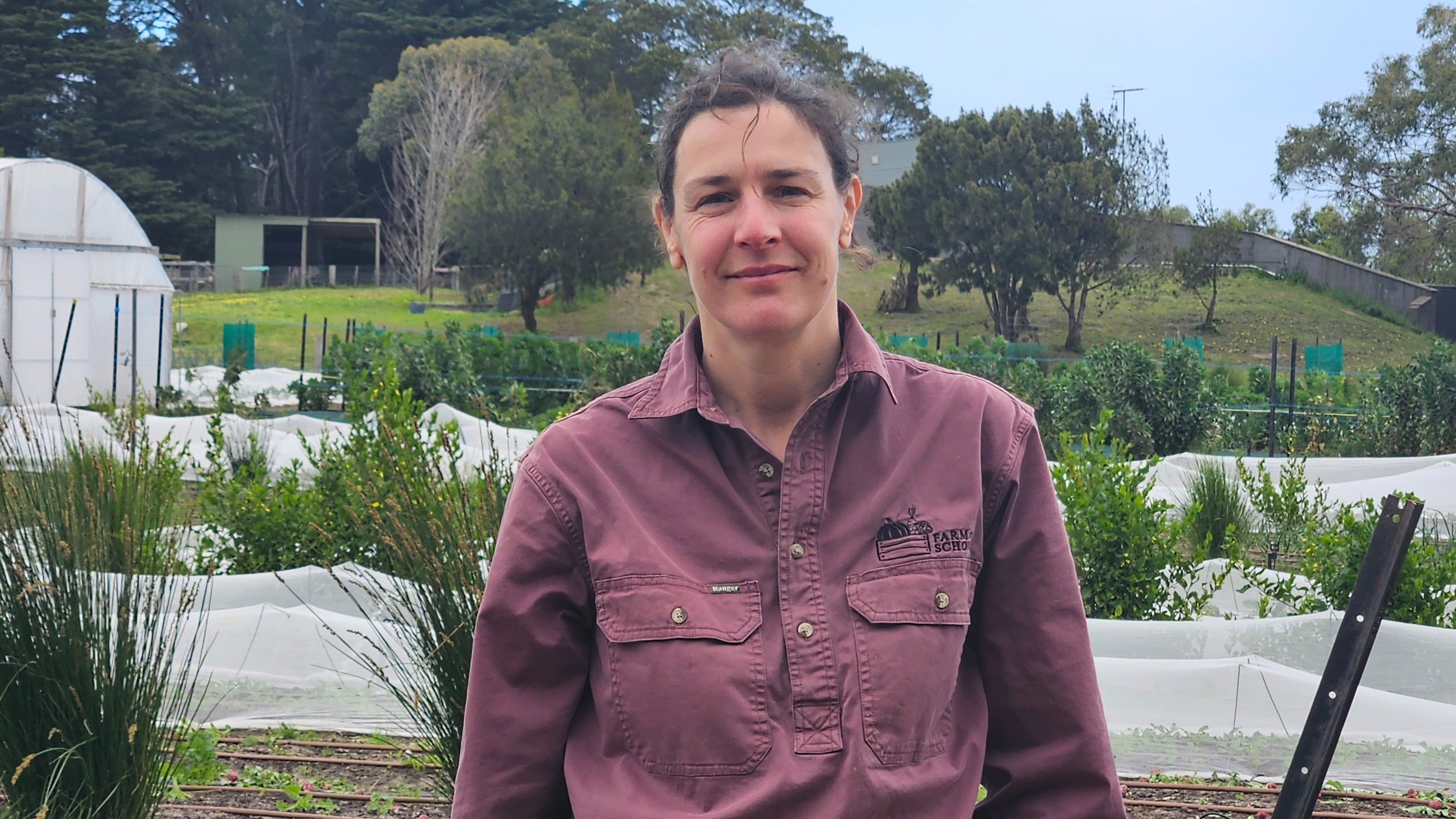 Farm My School Education Manager Tracey Gibbs standing in the school market garden, surrounded by students and fresh produce beds.